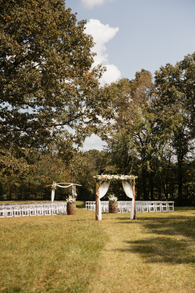 wider shot of outdoor ceremony set up with white folding chairs and gorgeous arches